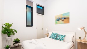 A neatly made bed with white linens, a blue patterned pillow, and a painting of a boat on the wall. - Slick Home, Free Parking (Brunswick)