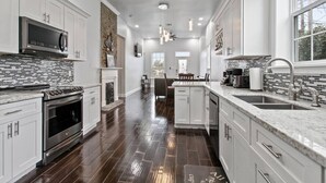 A modern kitchen with white cabinets, a built-in oven, a microwave, and a large island with a sink.