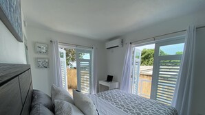Une chambre à coucher avec un lit, une table de chevet sur laquelle se trouve un ordinateur portable, et une vue sur l’extérieur grâce à une porte coulissante.