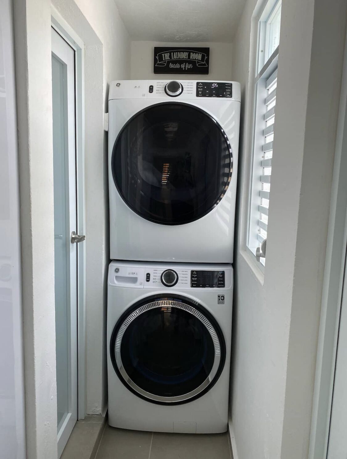 A laundry room with two stacked washing machines and a sign above them.