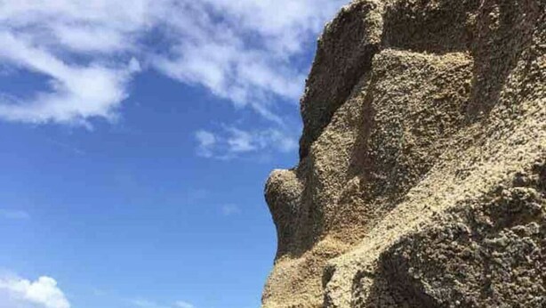 Une plage avec une grande formation rocheuse et un ciel dégagé.