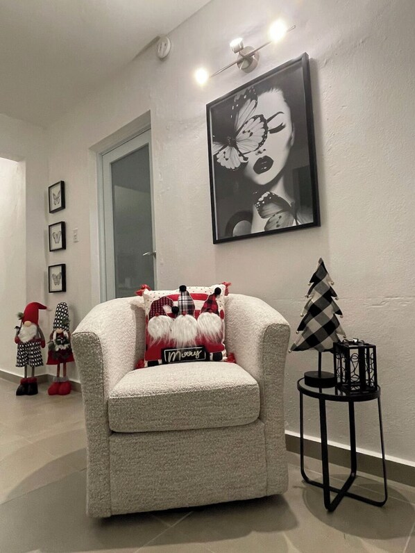 A modern living room with a white armchair, a black and white checkered Christmas tree, and a framed artwork on the wall.