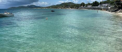 A beach with clear turquoise water, a boat, and distant hills.
