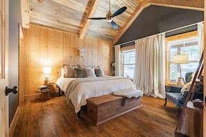 Une chambre dans une cabane en bois, avec un lit, une table de chevet, une lampe, un banc et une fenêtre avec des rideaux.