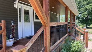 A wooden porch with a staircase leading to a deck, a white door, and a bird feeder.