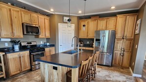 A spacious kitchen with wooden cabinets, a central island, stainless steel appliances, and a tiled floor.