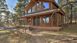 Eine Holzhütte mit Veranda, großen Fenstern und einem Metalldach, umgeben von Bäumen.