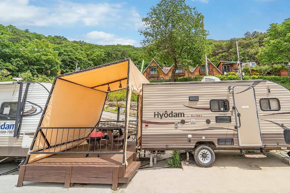 Una caravana Hyodam con un toldo grande y una terraza de madera adosada.