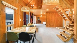 Ein Holzblockhaus-Interieur mit Essbereich, einer Treppe und Blick durch ein Fenster.