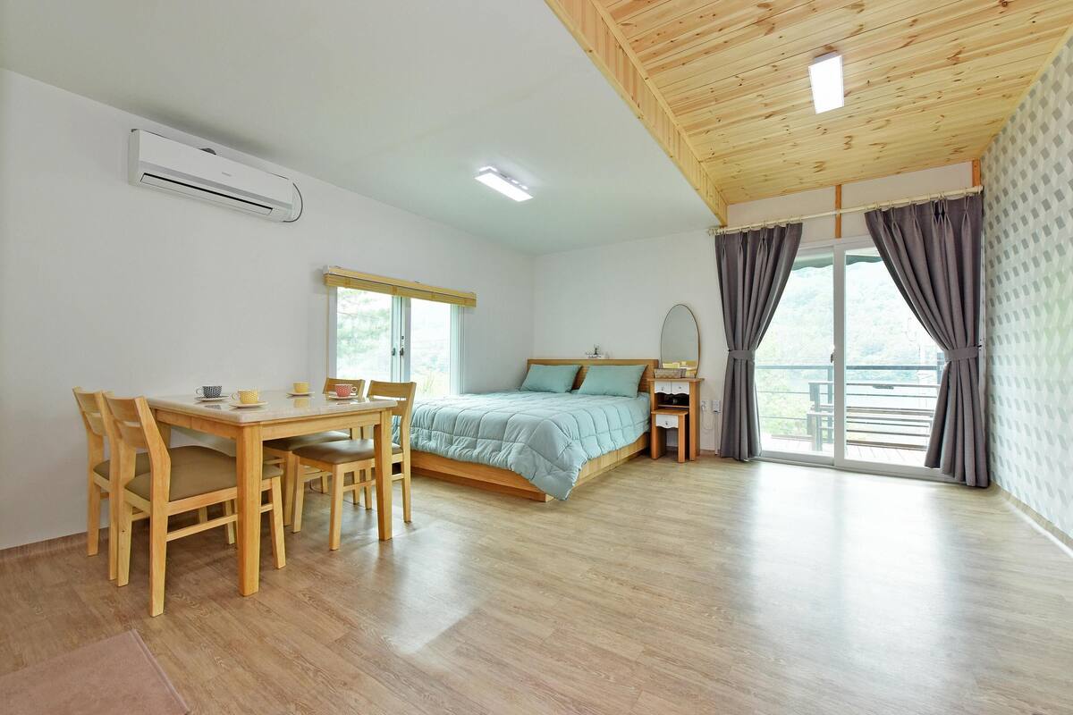 Una habitación con cama, escritorio, sillas, ventana y balcón.