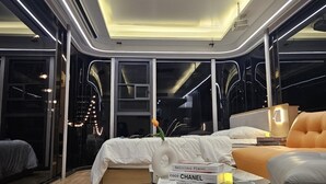 Ein modernes Hotelzimmer mit Oberlicht, einem runden Glastisch, einem Bett und einer Couch.