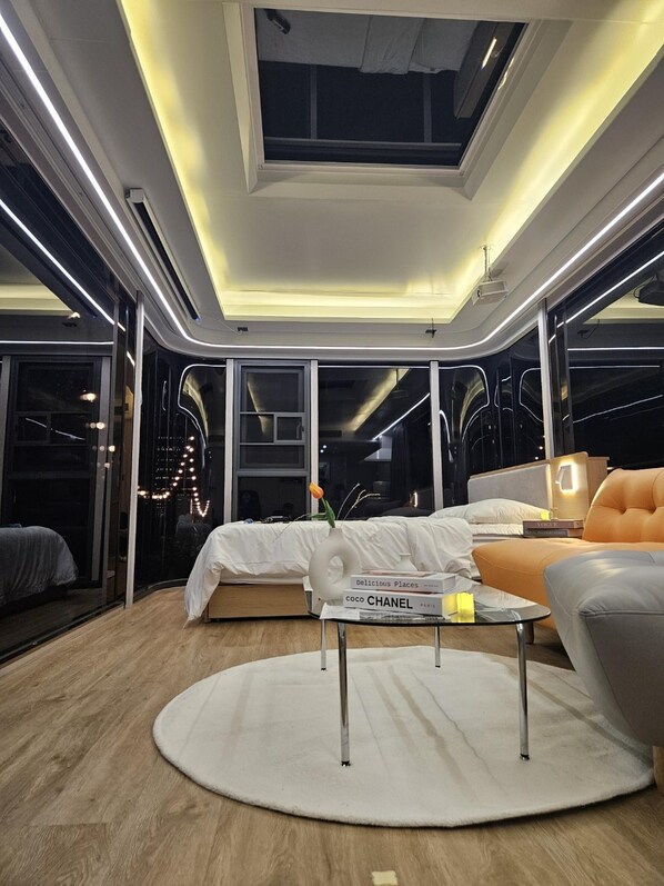 Una habitación de hotel moderna con tragaluz, una mesa redonda de vidrio, una cama y un sofá.