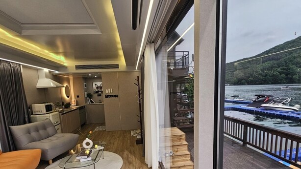 Ein modernes Hotelzimmer mit großem Fenster, einem Balkon mit Blick auf Boote und einer gemütlichen Sitzecke mit Sofa und Couchtisch.