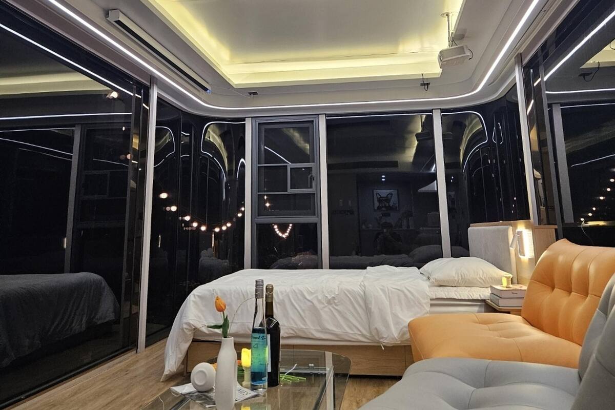 Un interior moderno con una cama, sofá y mesa de vidrio, con ventanas amplias y tragaluces.