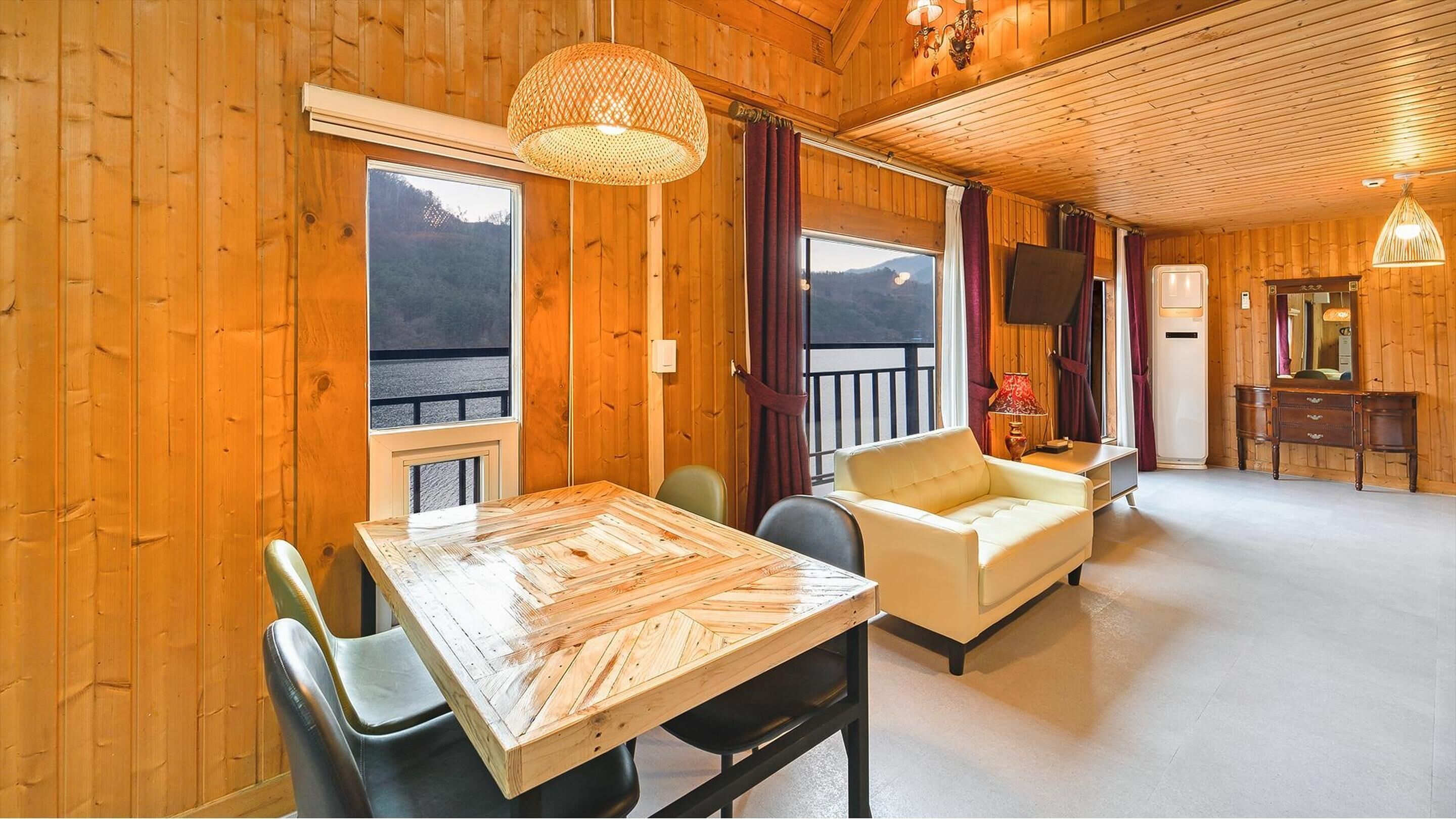 L’intérieur d’un chalet en bois comprend une table à manger, deux chaises, un canapé, un téléviseur et une commode.
