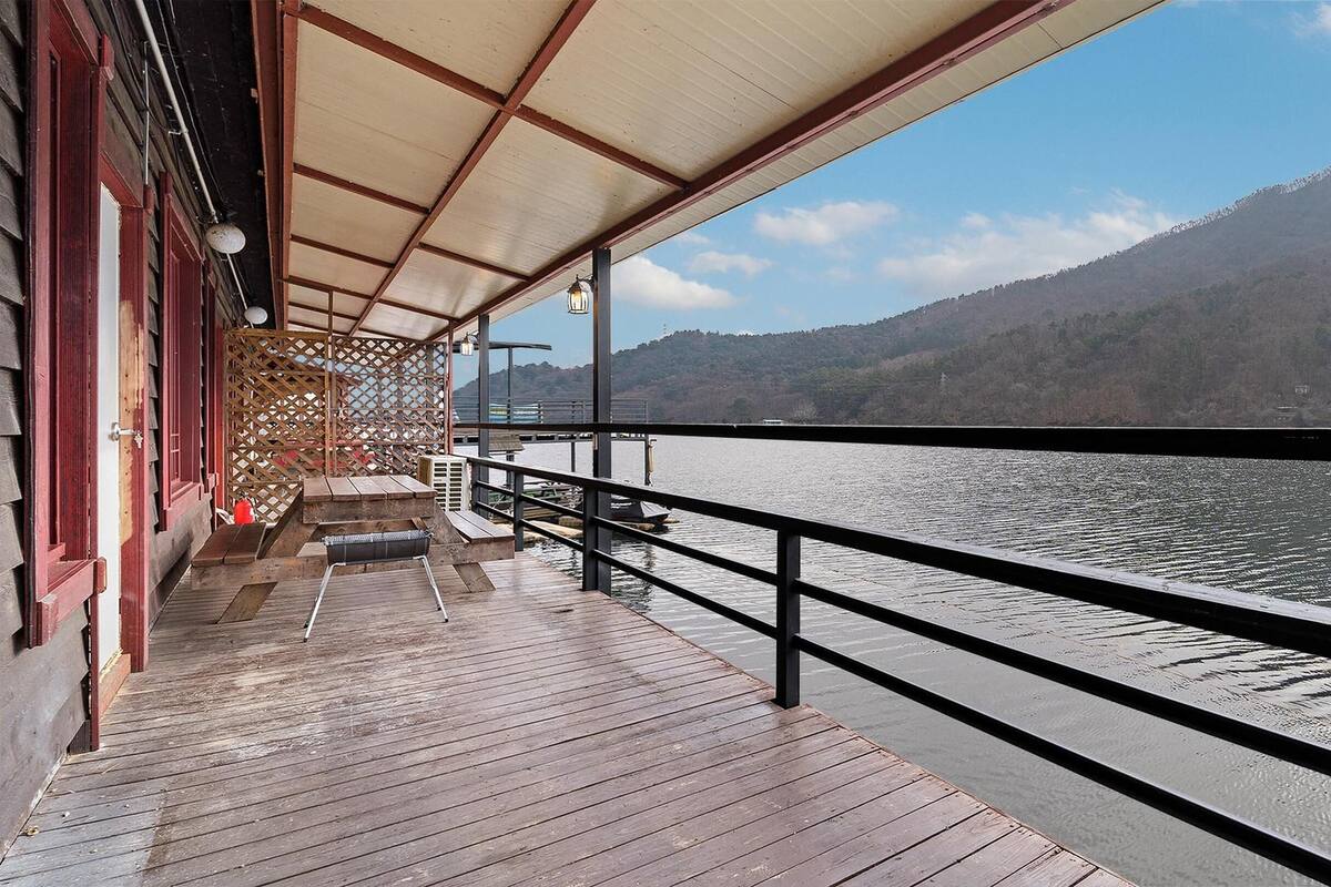Terraza de madera con barandal metálico que da a un lago tranquilo, con una montaña al fondo.