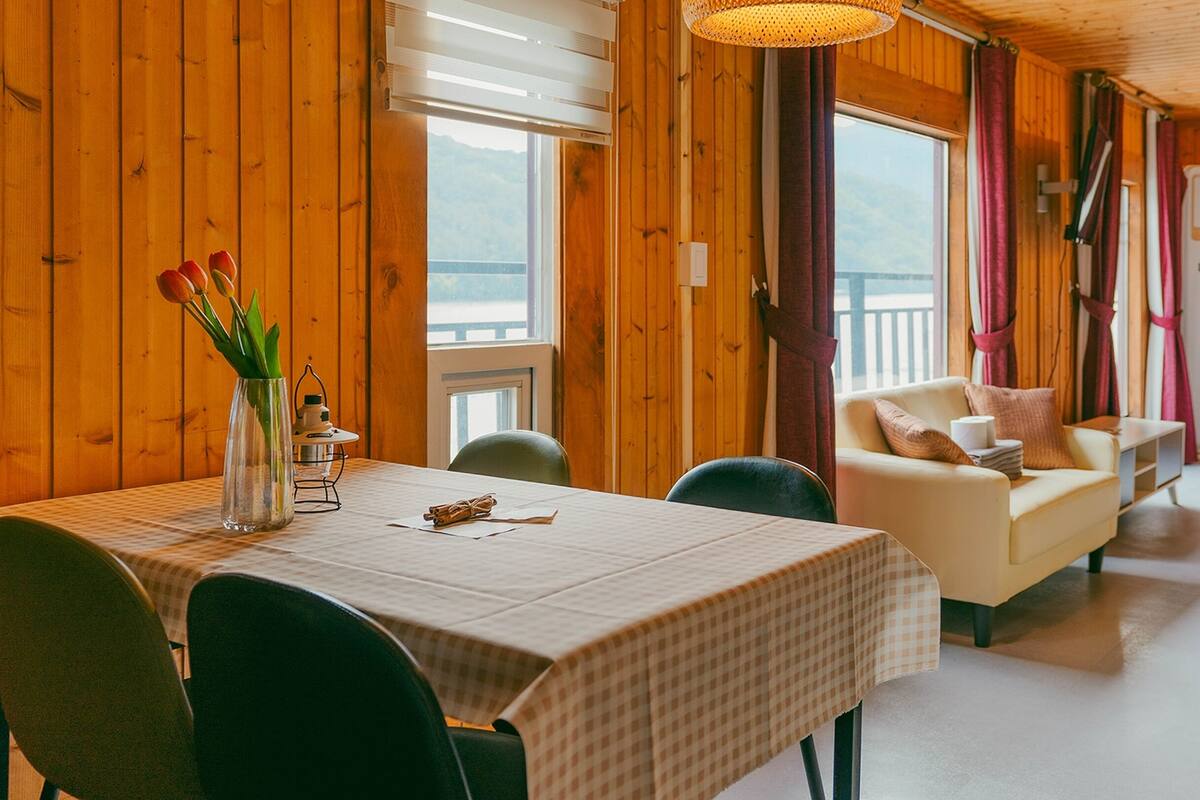 Un interior de madera con una mesa de comedor, sillas, un sofá y vistas al exterior.