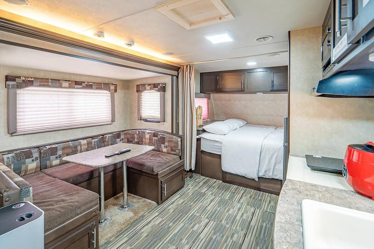 Interior compacto de una caravana con kitchenette, zona de comedor y litera.