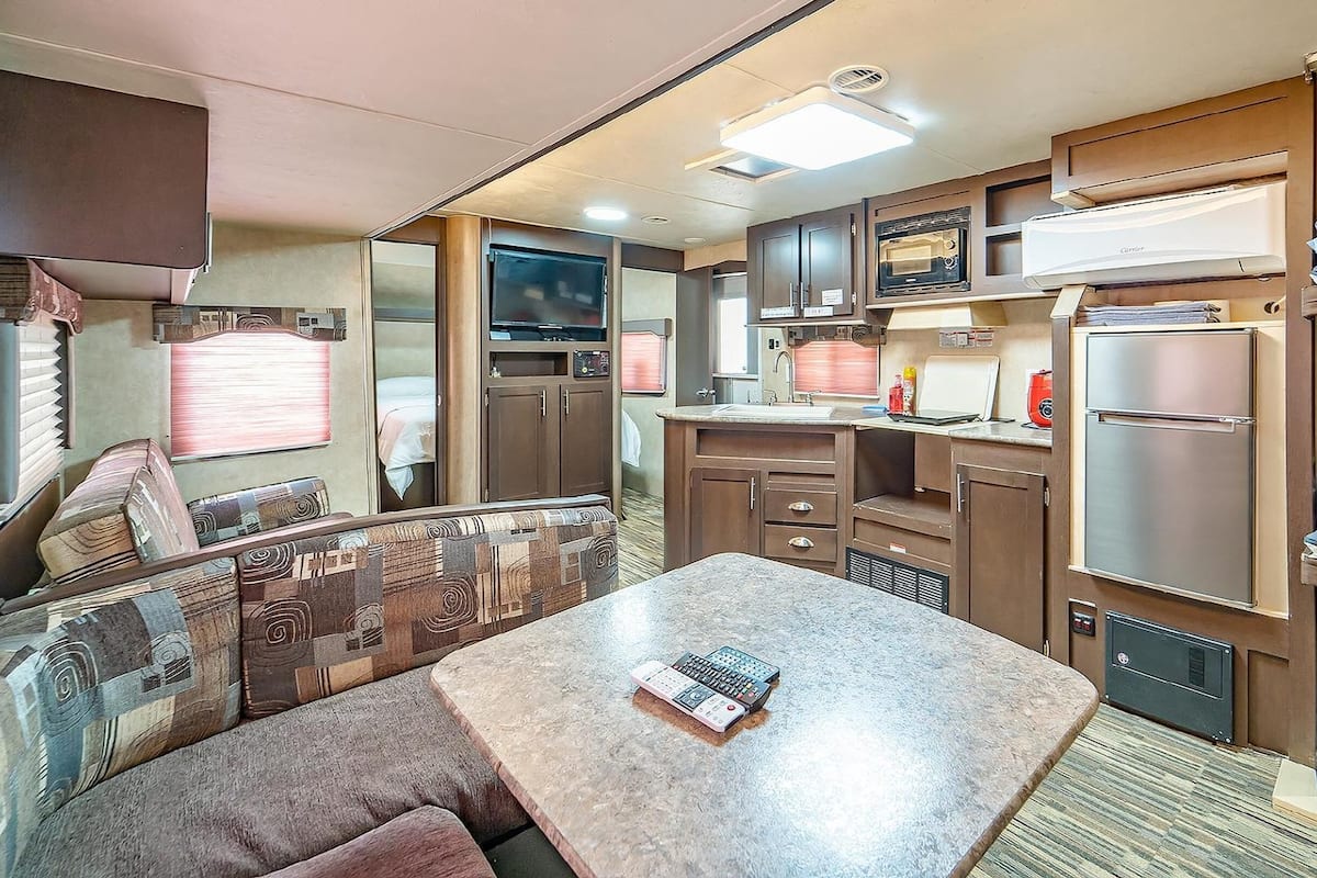 Interior compacto de una caravana con kitchenette, zona de comedor y espacio para dormir.