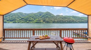 A wooden deck with a table set for a meal, overlooking a lake with mountains in the background. - Gapyeong Leupuang Pension (Gapyeong)