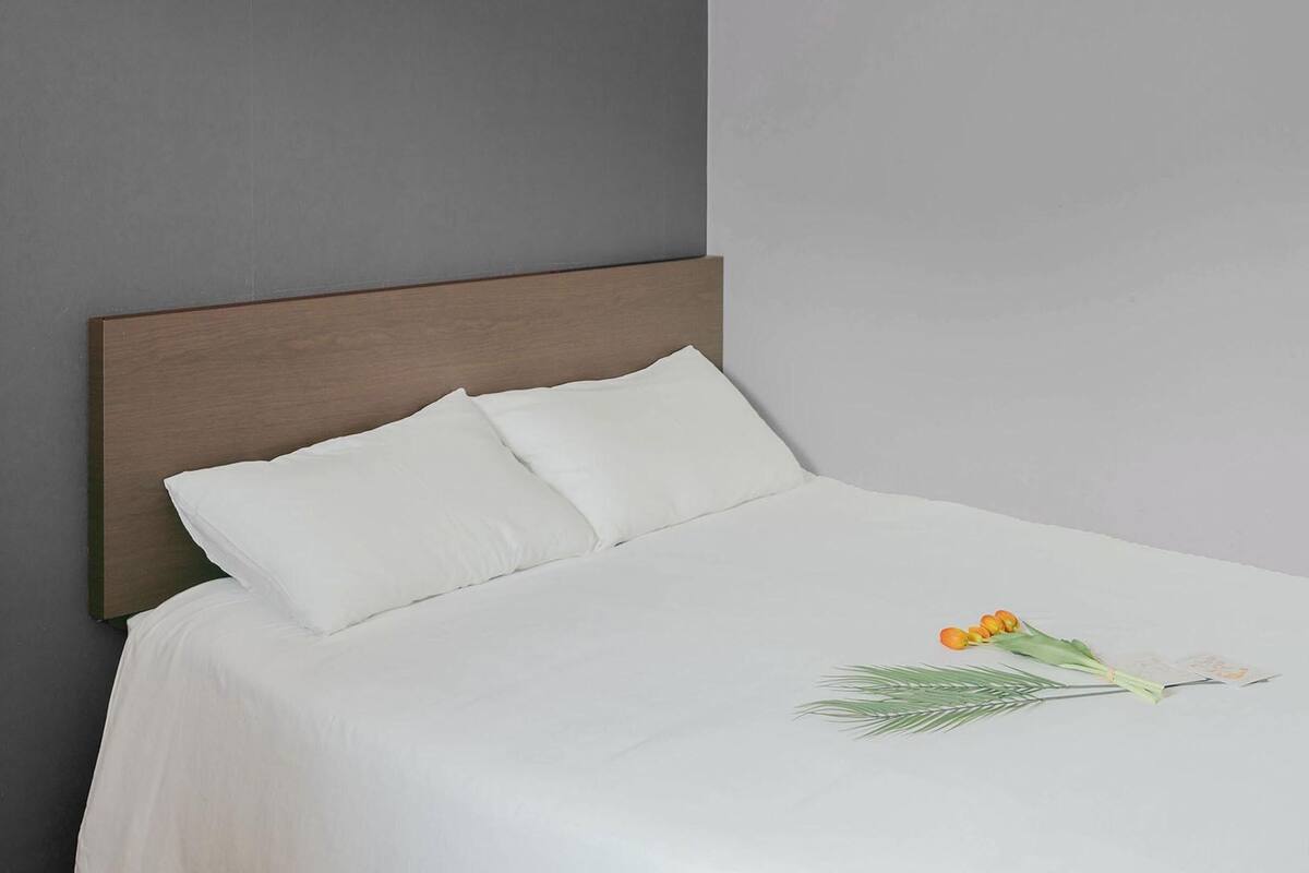 Una cama bien hecha con ropa blanca y un cabecero de madera, un ramo de flores y un interruptor de luz en la pared.