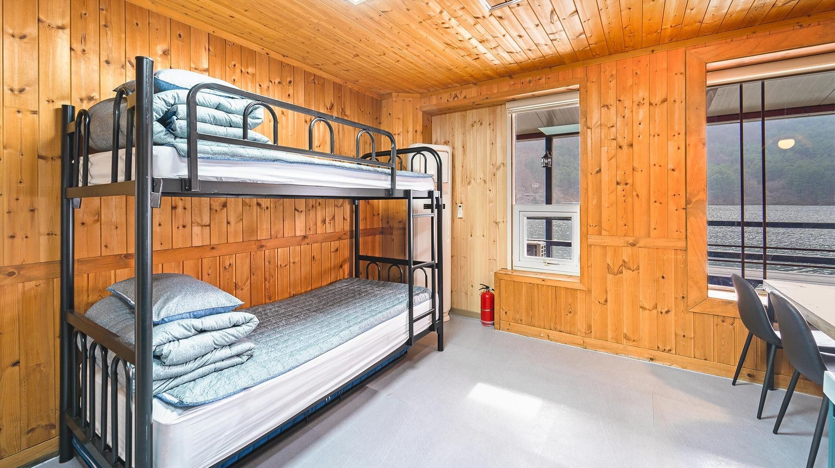 Habitación con literas, paredes de madera y ventana con vista a un cuerpo de agua.