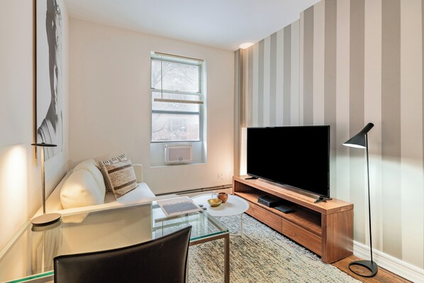 Una sala de estar moderna con una mesa de vidrio, un sofá blanco, un televisor de pantalla plana sobre un mueble de madera y una pared a rayas.