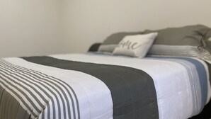 A neatly made bed with striped bedding and a pillow with the word "home" on it.