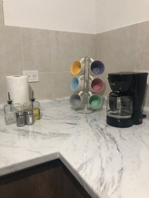 A kitchen with a marble countertop, a coffee maker, a mug rack, and various kitchen items.
