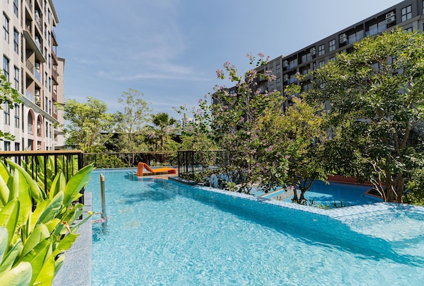 A swimming pool surrounded by lush greenery and modern buildings.