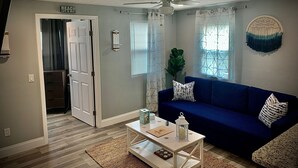 Ein Wohnzimmer mit blauem Sofa, weißem Couchtisch und Deckenventilator.