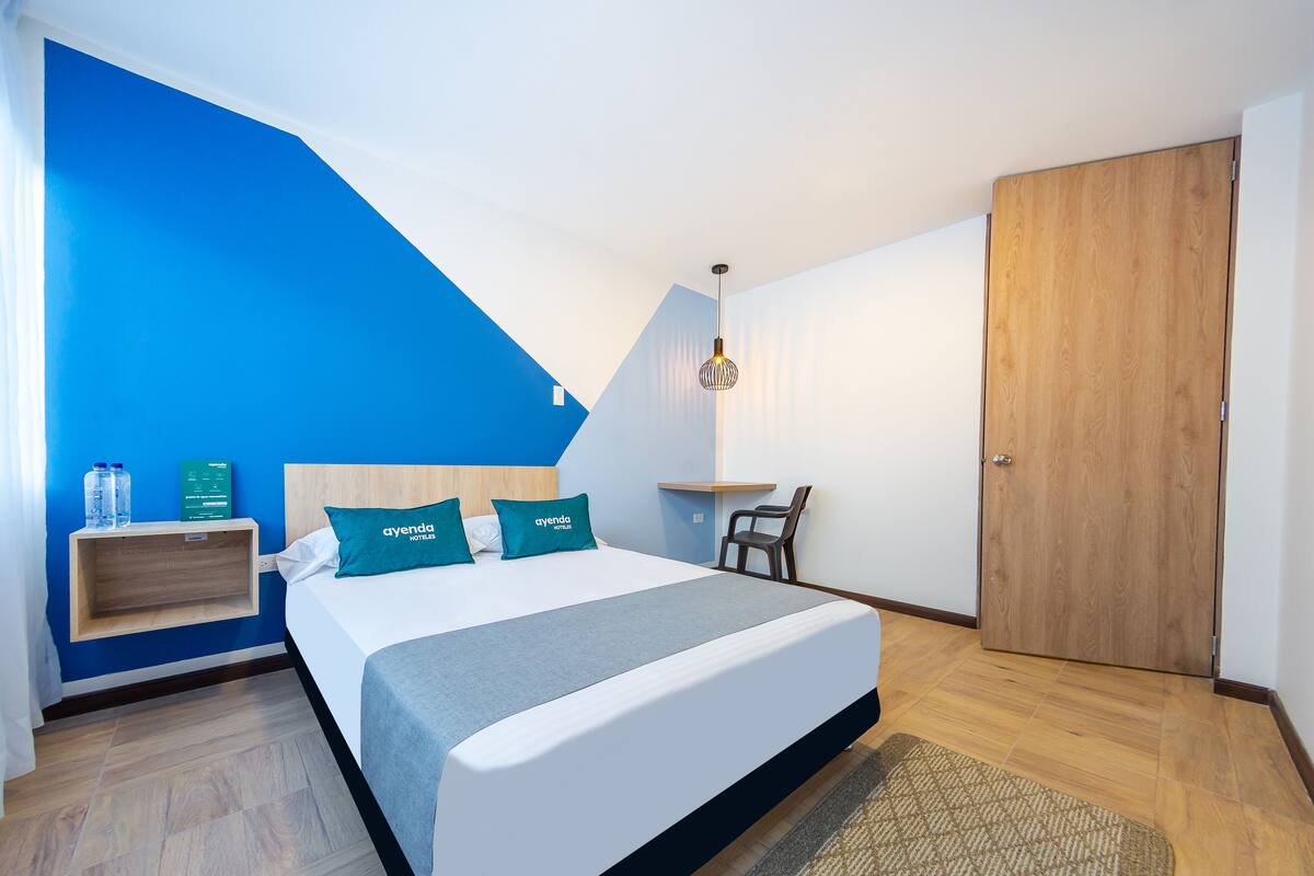A modern hotel room with a bed, a desk, and a wardrobe.