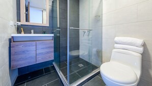 A modern bathroom with a glass-enclosed shower, a wooden vanity, and a white toilet.