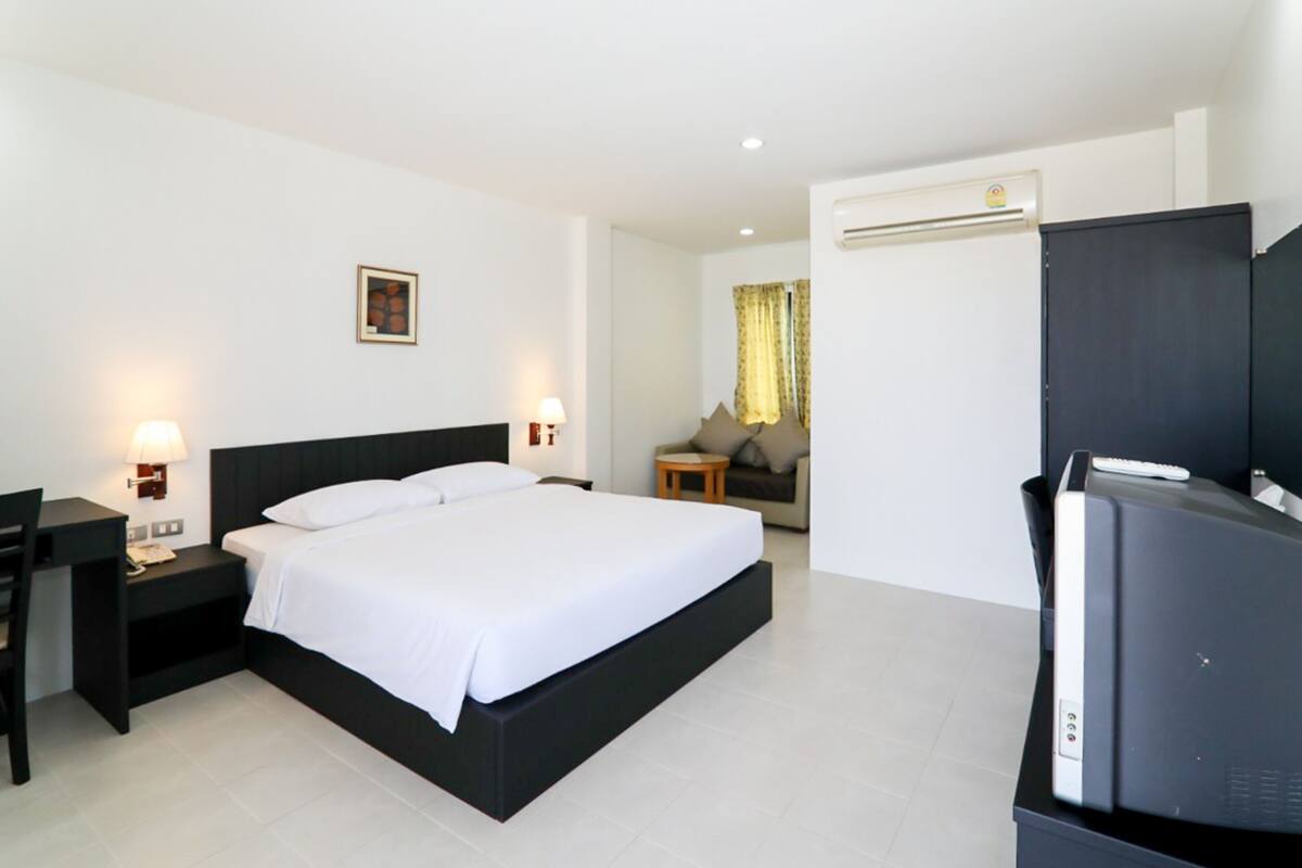 A hotel room with a single bed, a desk with a chair, a television, and a small table with a lamp.