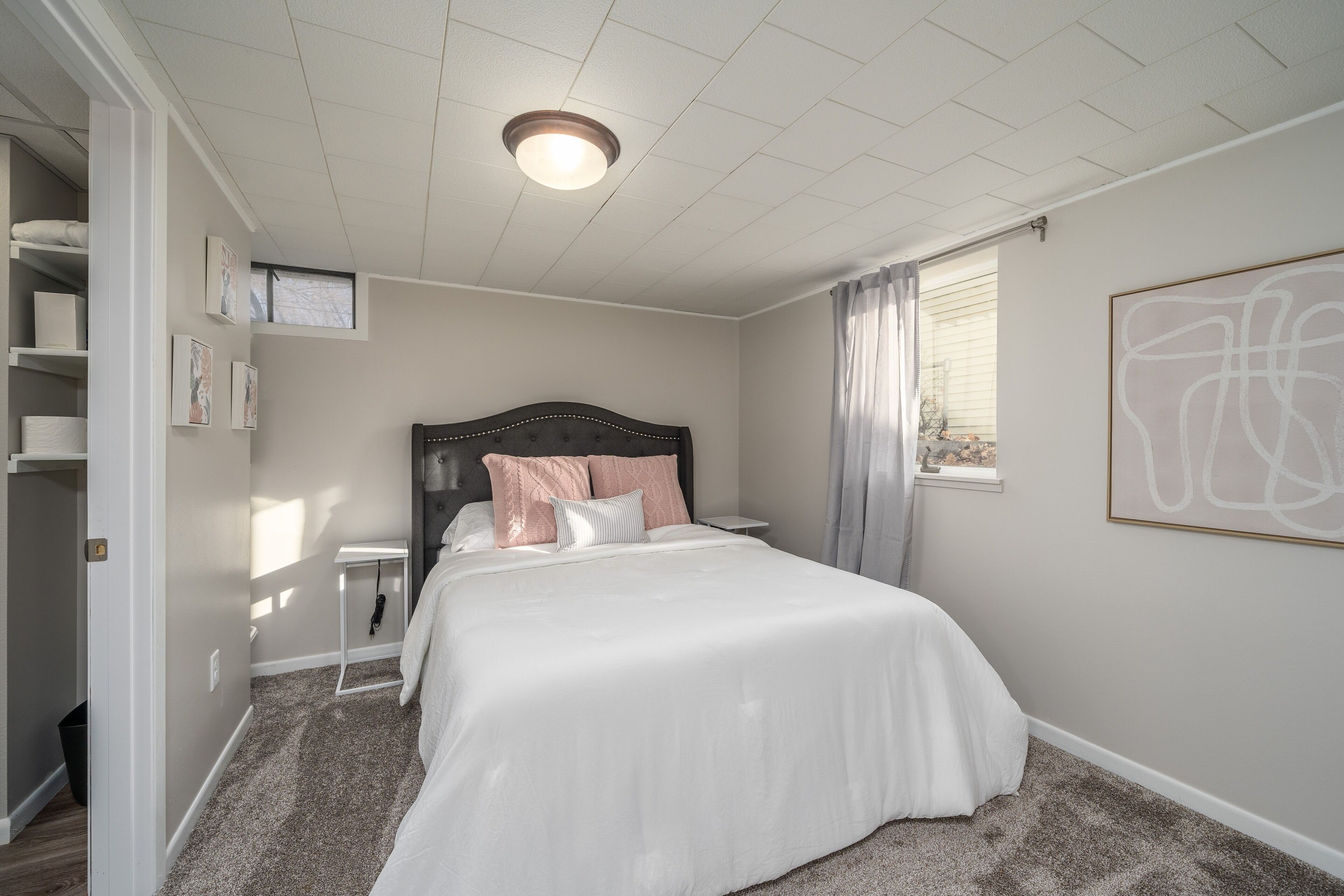 A bedroom with a large bed, a bedside table, a nightstand, a window with curtains, and a ceiling light.