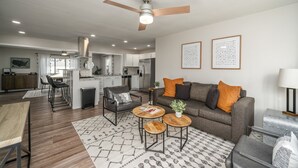 A modern living room with a grey sofa, a coffee table, and a dining area with a wooden table. - Five Star Flip- Bright & Renovated 3BR/2BA (Sioux Falls)