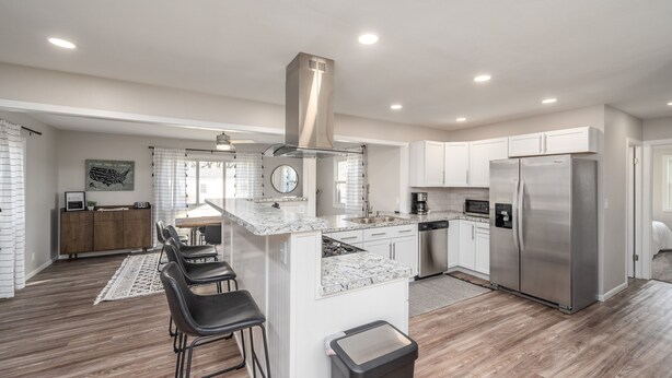 A modern kitchen with a central island, stainless steel appliances, and a dining area with bar stools. - Five Star Flip- Bright & Renovated 3BR/2BA (Sioux Falls)