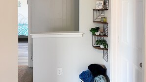 Ein Flur mit einer weißen Tür, einem Wäschekorb und einem an der Wand befestigten Regal mit Pflanzen und Dekoration.