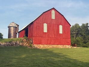 Ein rotes Bauernhaus mit einem Silo, umgeben von einer Steinmauer und einem grünen Feld.