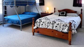 Una habitación con literas, una cama de madera, ventilador de techo y mesita de noche con lámpara.