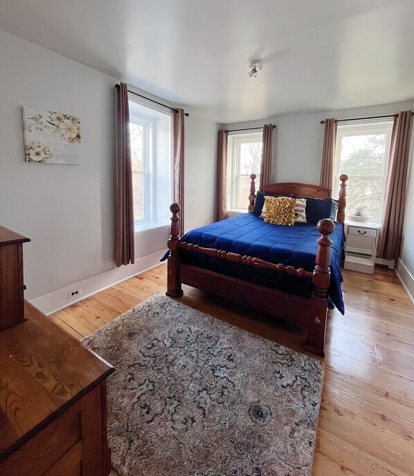 A bedroom with a wooden bed, a nightstand, a dresser, and a large window with curtains.