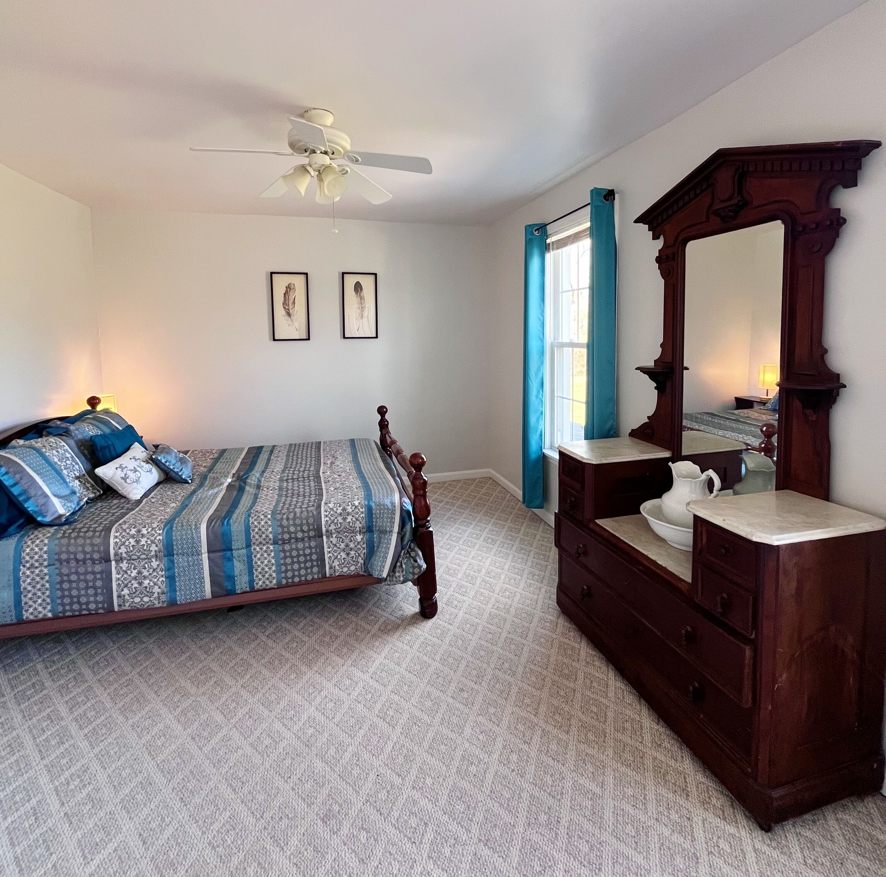 A bedroom with a bed, dresser, mirror, ceiling fan, and two framed pictures on the wall.