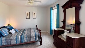 Ein Schlafzimmer mit Bett, Schminktisch, Spiegel, Deckenventilator und zwei gerahmten Bildern an der Wand.