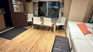 A living room with a wooden floor, a white sofa, a black ottoman, and a glass-top dining table with chairs. - Bay Mount Chalet with Sauna (Meaford)