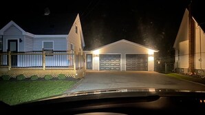 Una casa residencial de noche con un garaje bien iluminado y un patio delantero visible.