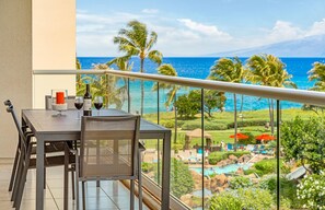 A balcony with a table set for two, overlooking a pool and a view of the ocean.