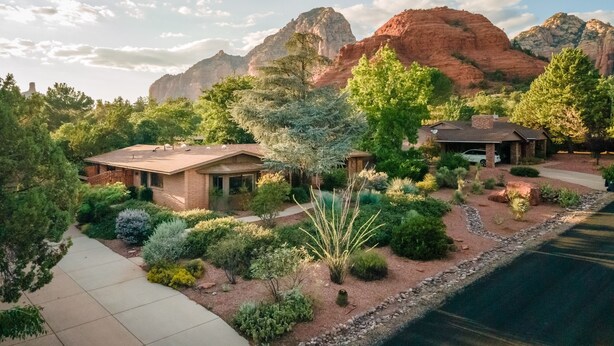 A house with a patio, surrounded by various plants and trees, with mountains in the background. - Sedona Serene Retreat, Amazing Views & Hot Tub! Walk to Hiking Trails!  (Sedona)