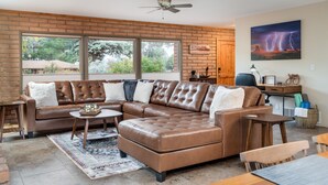 A modern living room with a brown leather sectional sofa, a coffee table, and a dining area with a wooden table and chairs. - Sedona Serene Retreat, Amazing Views & Hot Tub! Walk to Hiking Trails!  (Sedona)