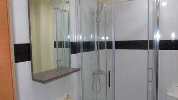 A bathroom with a glass-enclosed shower, a mirror above the sink, and a toilet.