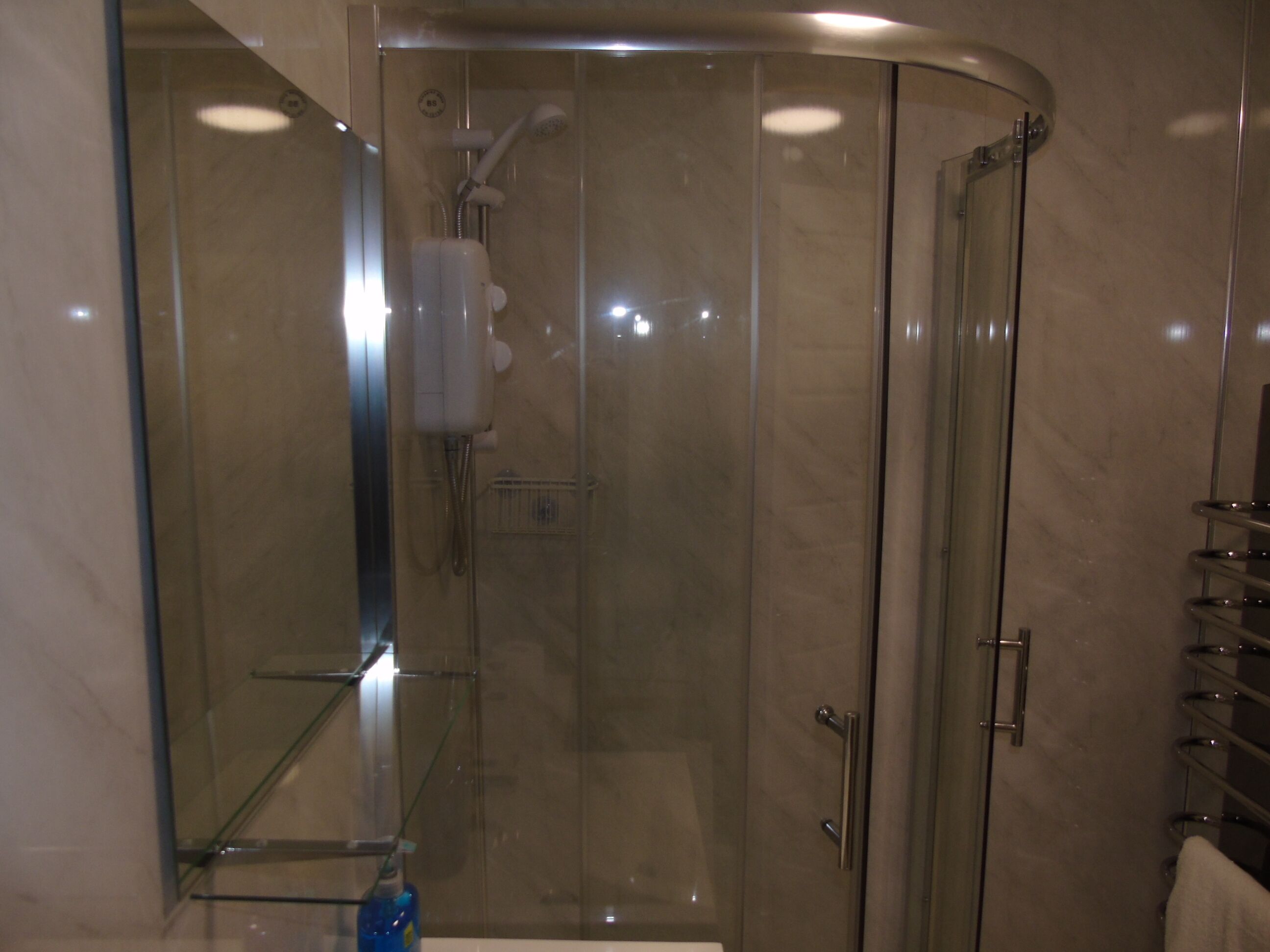 Ein modernes Badezimmer mit einer Glaskabine zur Dusche, einem Glastregal und einem Handtuchhalter aus Metall.